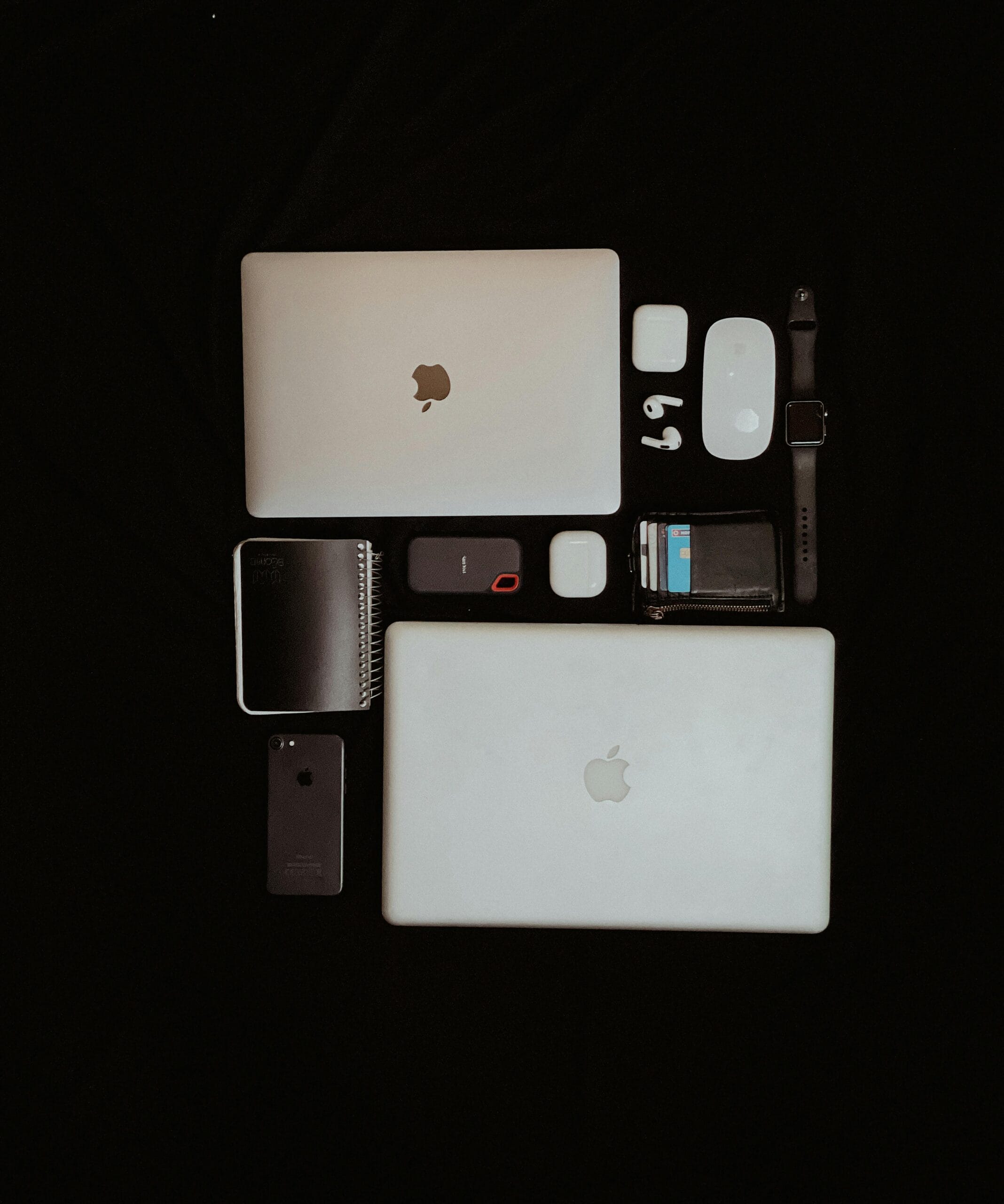 Top view of modern apple electronics including laptops, smartphone, and accessories on a dark background.