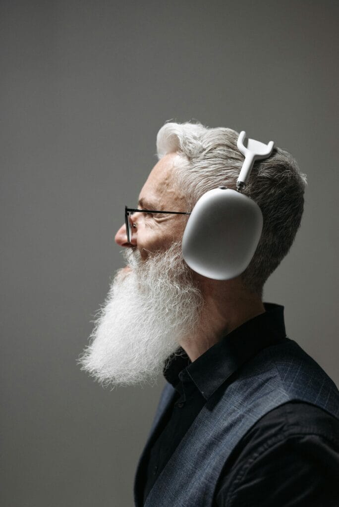 Side profile portrait of a mature man with a beard and wireless headphones against a neutral background.