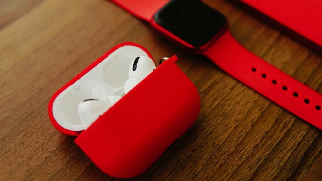 Close-up of red AirPods and smartwatch on wooden surface for modern tech enthusiasts.