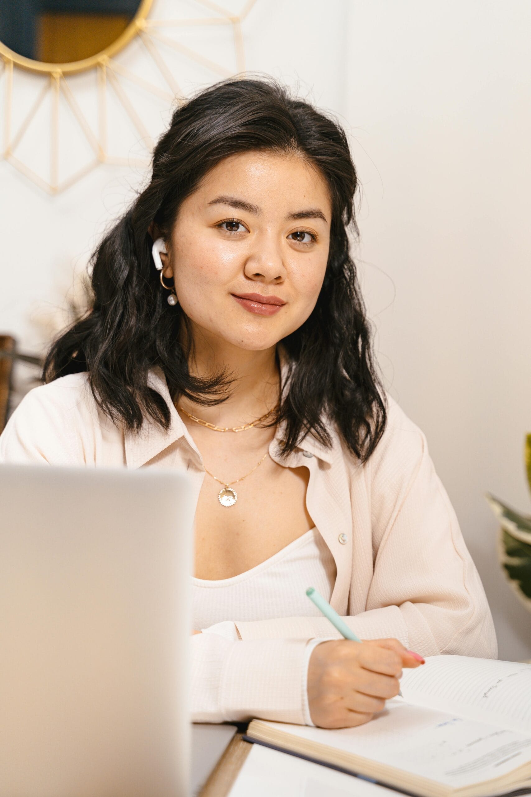 Young Asian woman using laptop and taking notes at home office desk.